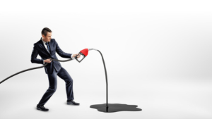 A businessman on white background holding a new red gas nozzle that's leaking oil to a large black puddle.