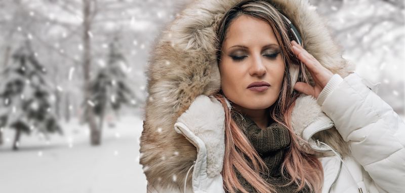 woman in winter with headphones on snowy background