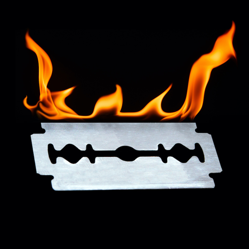 frontal studio photography of a shiny sharp razor blade with flames