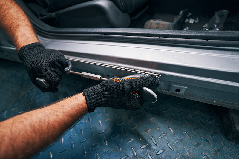 Technician putting tool for flattening of car parts against the metal surface below automobile side door