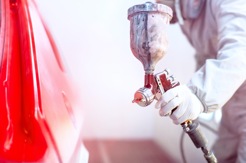 Close-up of spray gun with red paint painting a car in special booth