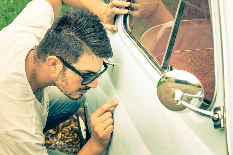 Young handsome man with sunglasses inspecting a vintage car body at second hand trade - Passion and transportation lifestyle of a retro classic vehicles collector