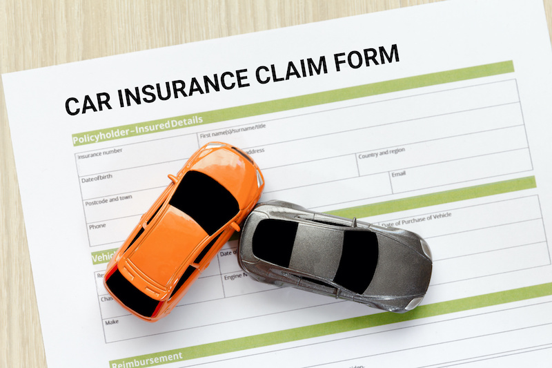 Top view of car insurance claim form with car toy crash on wooden desk