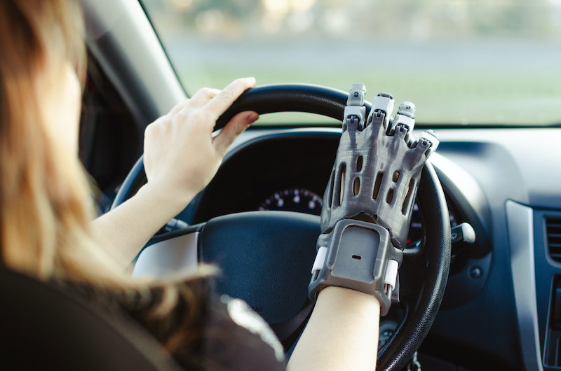 a woman with a prosthetic arm printed on a 3D printer drives a car.