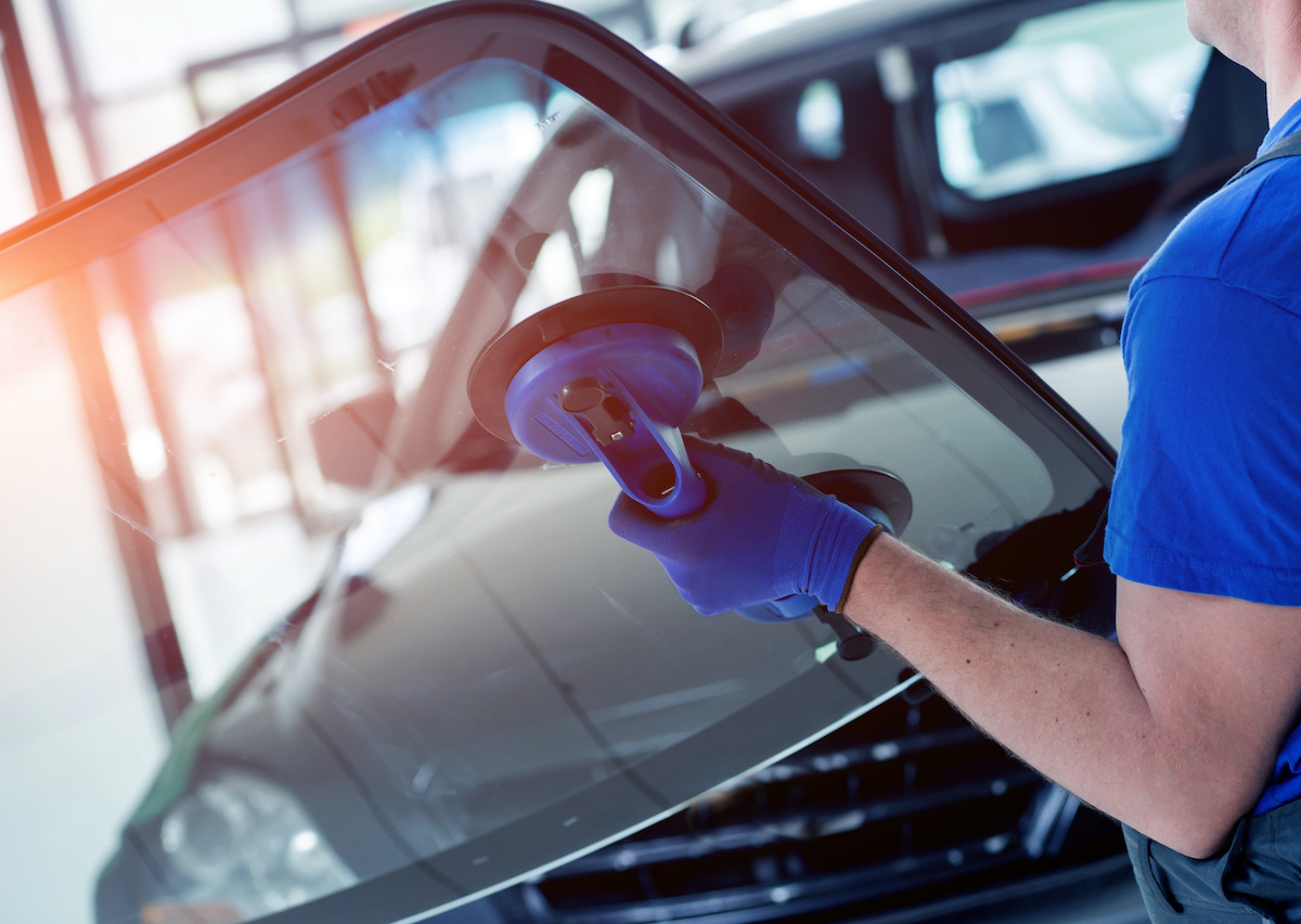 Automobile special workers replacing windscreen or windshield of a car in auto service station garage. Background