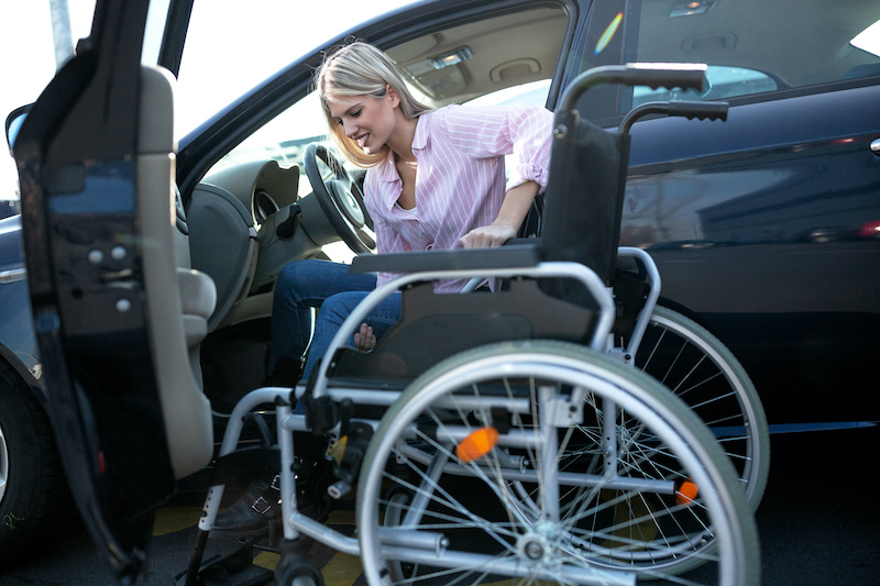 Physically challenged girl in pink shirt moving herself from the vehicle to the wheelchair on an outdoor parking