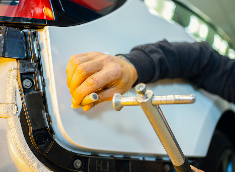 A specialist repairs a dent on the car body without painting. Process of paintless dent repair on car body. The mechanic at the auto shop with tools to repair dents in car body. Body repair. PDR.