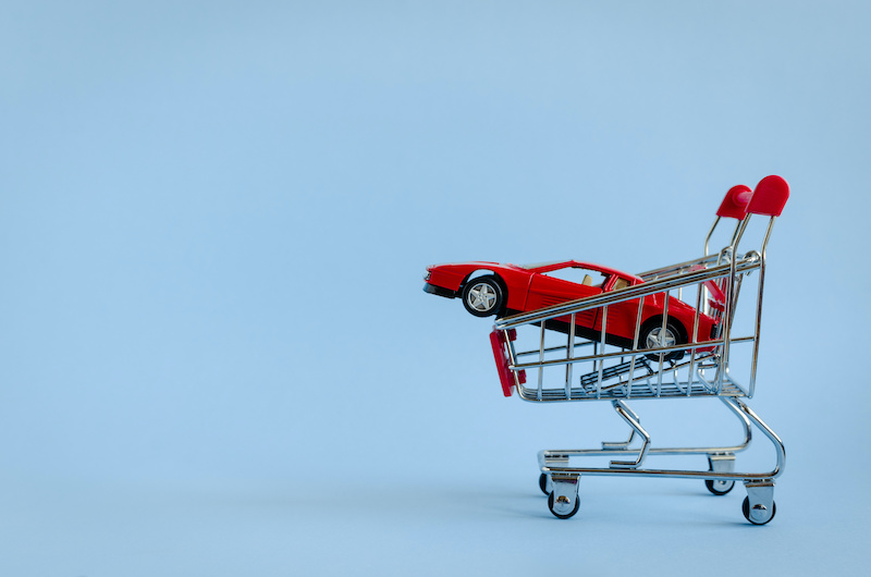 Car shopping concept. New red car in a shopping cart as a symbol for car buying and leasing. Blue background. Copy space.