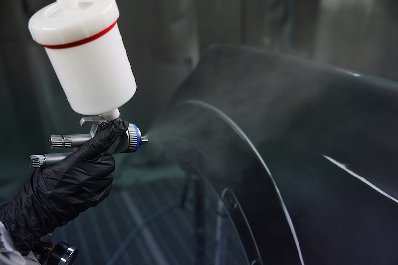 Cropped view of employee hand in protective glove painting car detail by using airbrush