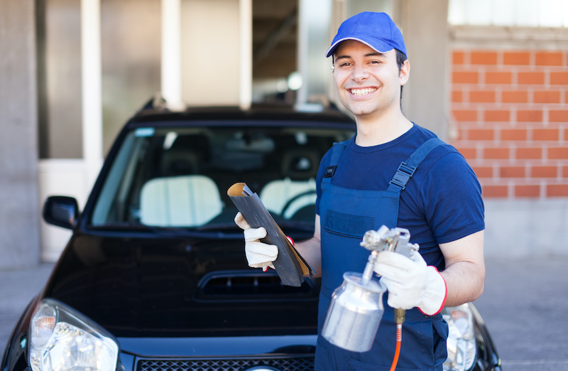 Car body repairer holding a spray gun and a sheet of sandpaper