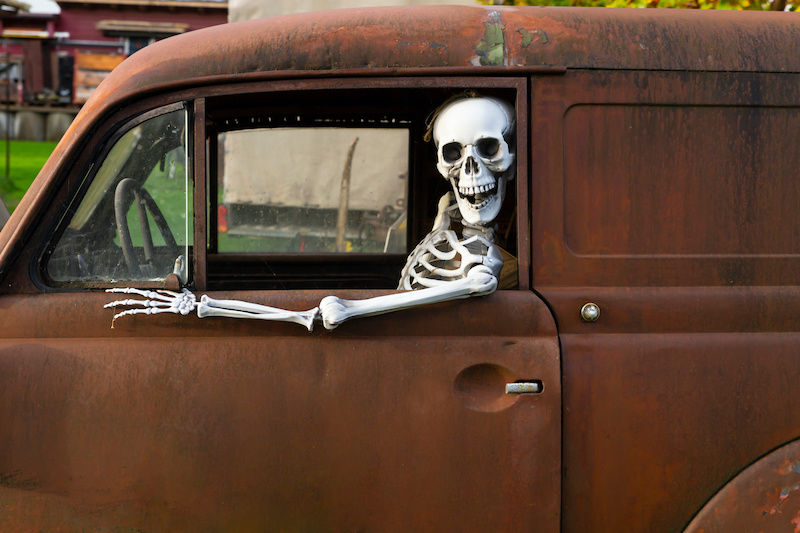 Human skeleton sitting in a rusty old car and looking out of the window