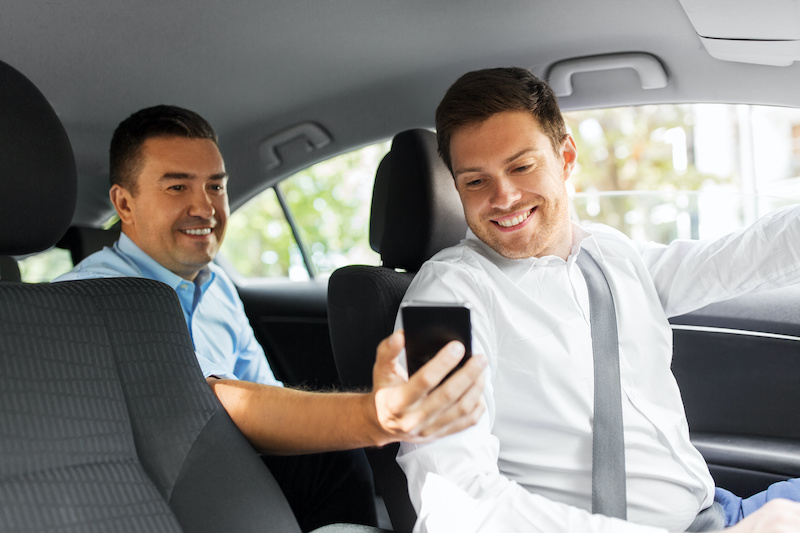 transportation, vehicle and technology concept - middle aged male passenger on back seat showing his smartphone to car driver