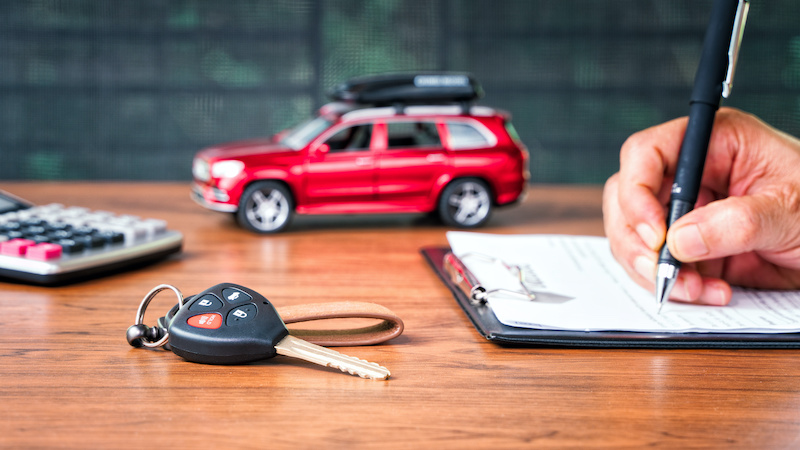 Car loan or buying a new car concept. Car key on table with a man signing on leasing or document  form and red car in background. Leasing and insurance business car accident checklist.