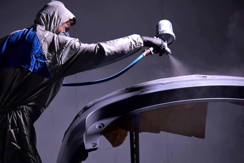 confident mechanic worker painting body of car in the service, wearing a full body costume and protection gear.