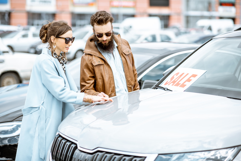 Young stylish couple choosing luxury car to buy on the open ground of the dealership