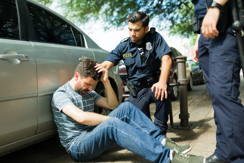 Injured young man suffering in pain after a car accident talking with the police officers