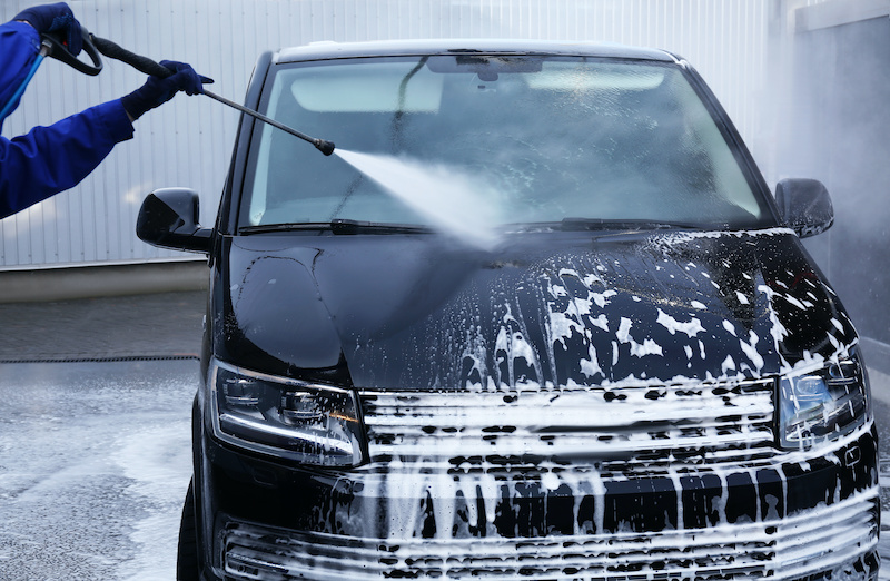 Worker cleaning automobile with high pressure water jet at car wash, closeup