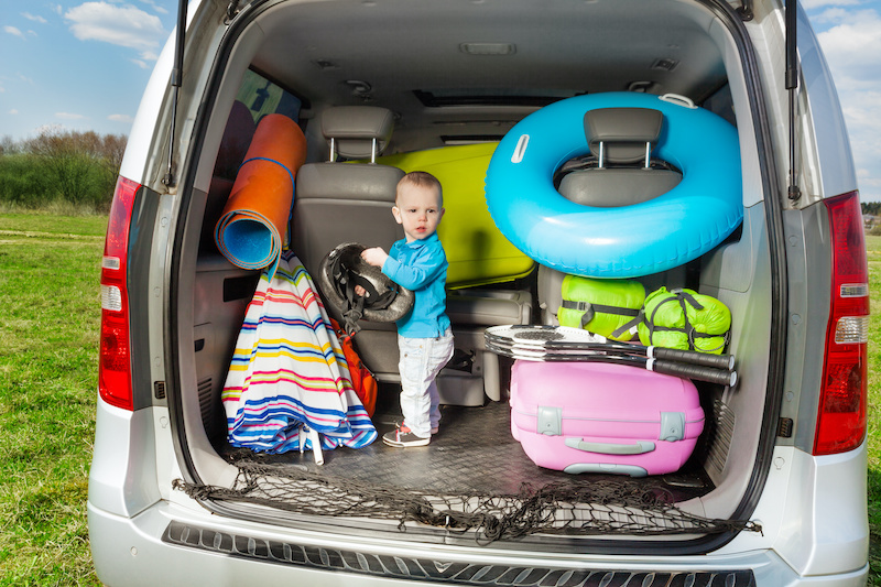 Cute little toddler packing luggage, standing in car boot, holding bike helmet