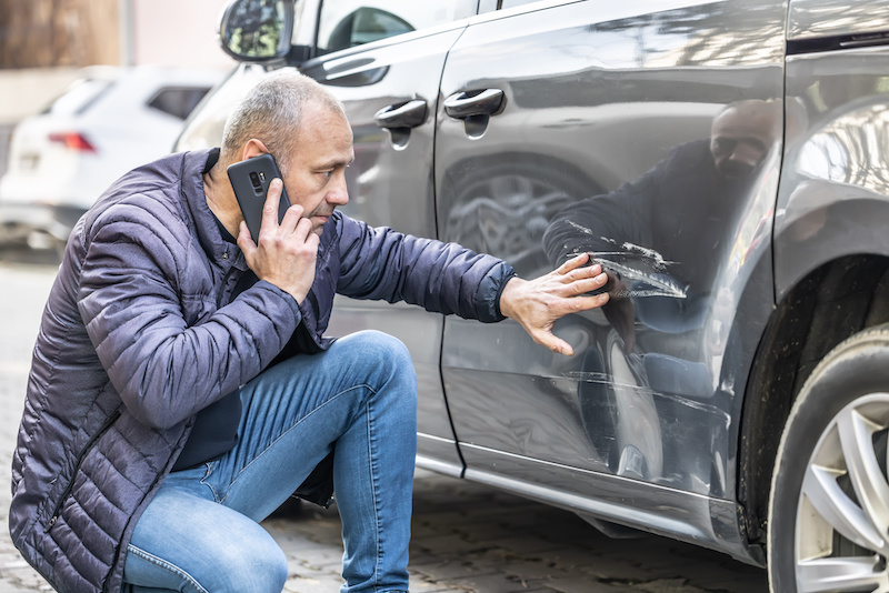 A man calls the insurance company or the police because someone backed into the side door of his car in the parking lot. car damage