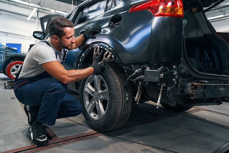 Concentrated light vehicle technician attaching screw clamps to car frame above rear wheel while flattening its surface