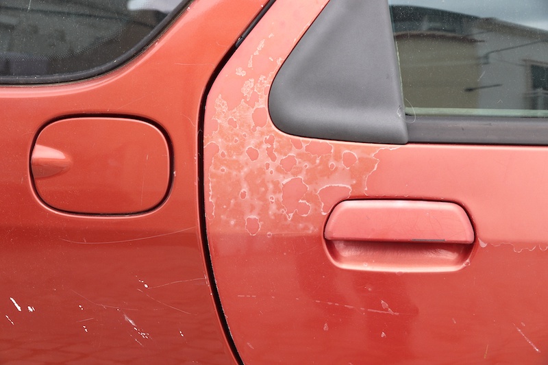 Faded car paint - peeling paint surface in a 20 year old European red car.