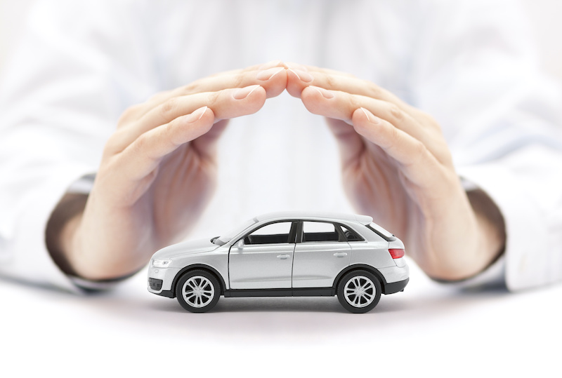 Car insurance. Small silver car covered by hands.