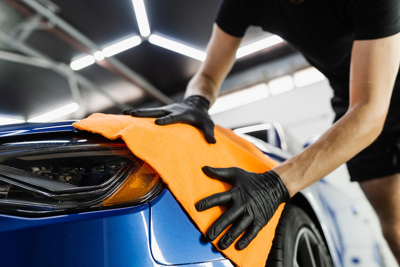 Hand car drying with microfiber in detailing auto service. Cleaner worker dry body car after washing automobile