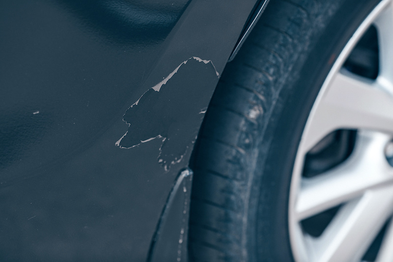 Hood of the black car with scratched and damaged paint peeled from the crash accident or collision close up