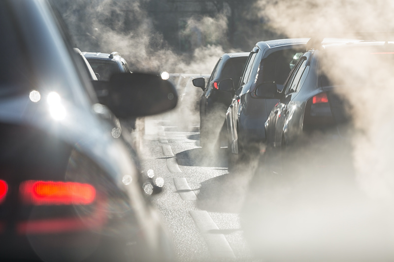 Blurred silhouettes of cars surrounded by steam from the exhaust pipes. Traffic jam