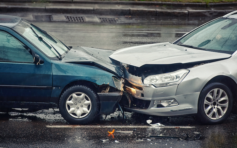 Car accident on wet road during rain, head on collision side view. Two cars damaged after head-on collision, car crash. Car crash on the street, damaged cars after collision. Traffic rules violation