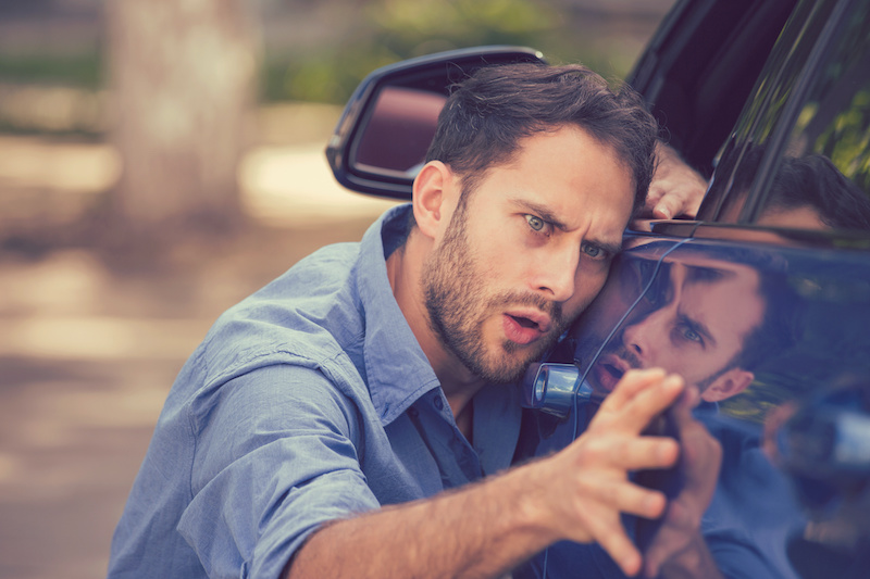 Young worried funny looking man obsessing about cleanliness of his new car on a summer day. Car care and protection concept