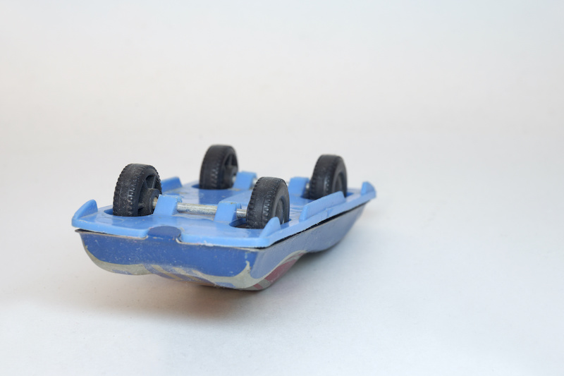 racing car. tin toy. laying on its roof rally toy car, showing plastic blue bottom and black wheels with tire tread pattern, on hidden axle