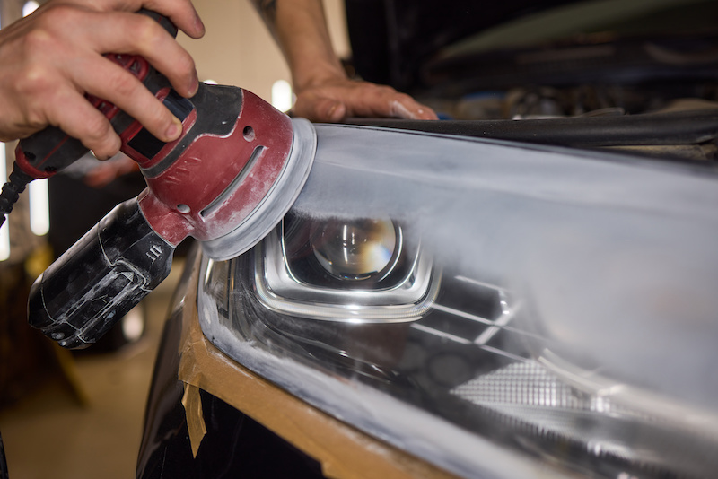 A person is using a machine to polish an automotive headlight, part of the vehicles lighting system, as part of automotive engineering maintenance