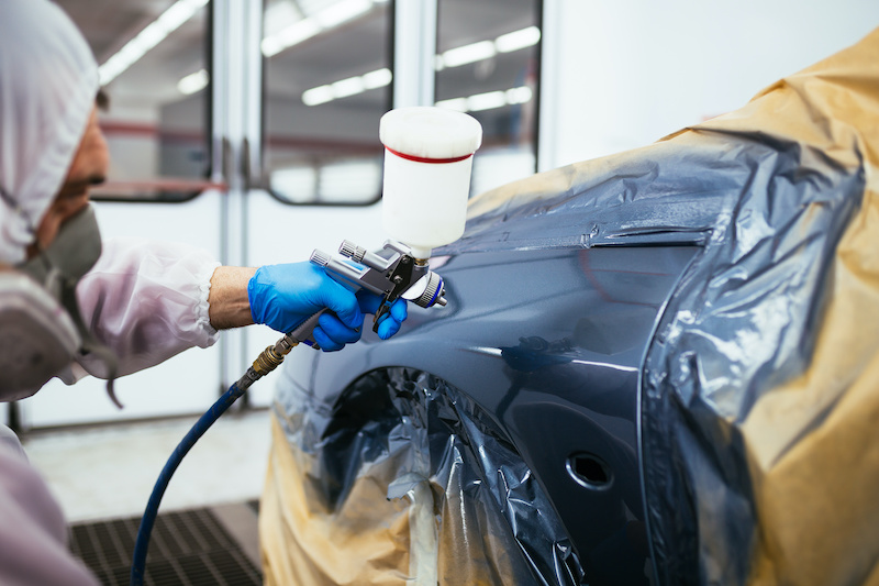 Man with protective clothes and mask painting car using spray compressor. Selective focus.