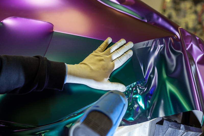 A specialist in wrapping a car with chameleon-colored vinyl film in the process of work. Car wrapping specialists cover the car with vinyl sheet or film. Selective focus.