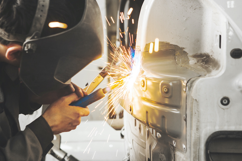 Worker in mask welds car in auto service of bodywork. Industrial concept of vehicle repair.