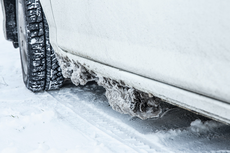 Detail view of frozen salt, snow and ice chunks stuck under car body, causes rust and corrosion in the winter outdoors.