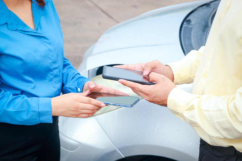 Man and woman use smartphones to exchange information for car insurance claims. Transport concept.