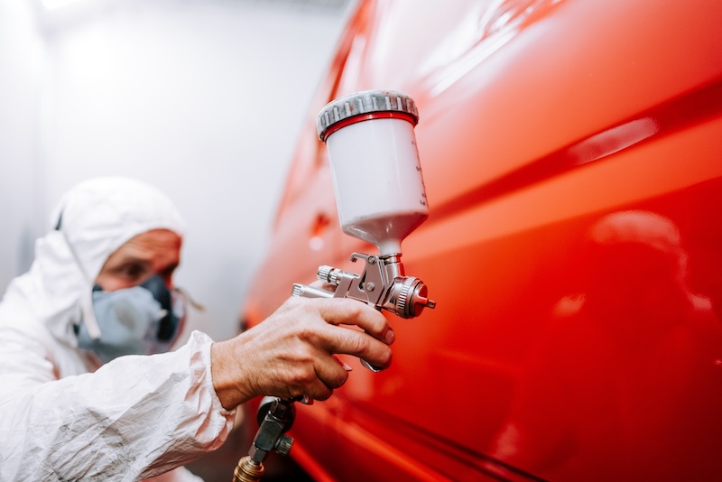 mechanic worker painting a car in a special painting box, wearing a full body costume and protection gear