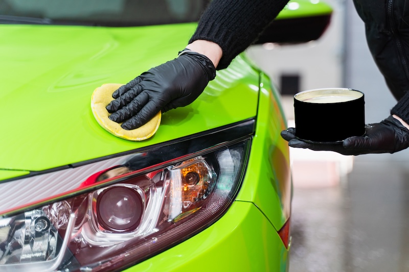 Hard wax for protection paintwork of car using sponge for remove paint scratches. Applying hard wax with a yellow sponge. Protection of paintwork.