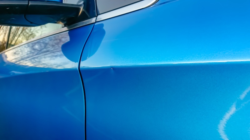 A small dent in the fender of a blue metallic car