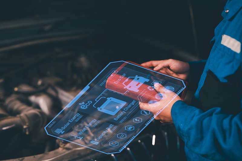 A technician uses augmented reality on a transparent tablet to analyze a car engine, displaying battery status and energy efficiency data.