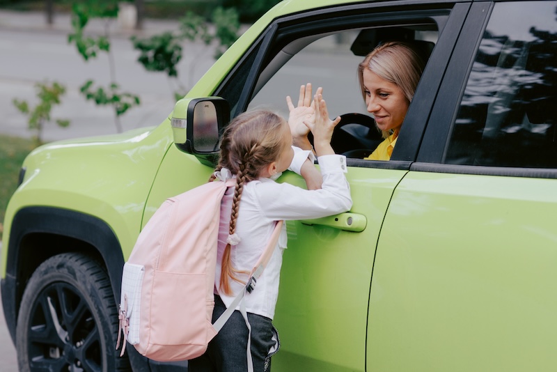 Mother and daughter share an emotional farewell through the car window on the first day back to school, showing encouragement and support.