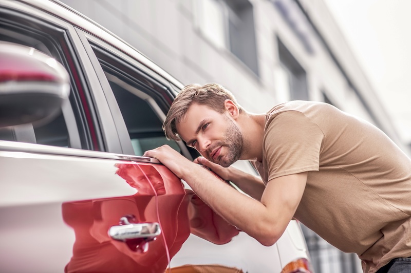 Brand-new car. Bearded young male bending, looking inside red car