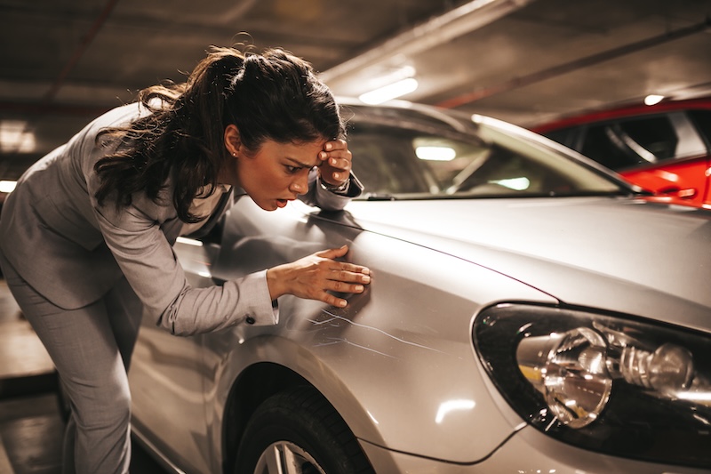 Frustrated and terrified young businesswoman looking at her scratched car.