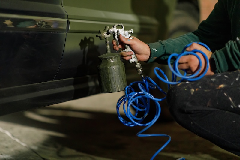 A person is using an airbrush to spray paint a car in a garage.