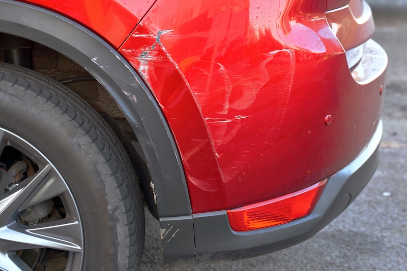 Close-up of scratched rear bumper on red car, visible paint damage, scuff marks, indicating need for maintenance, repair, and refinishing. Scratched car bumper with paint damage, need for body repair