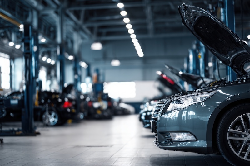Car repair shop, a grey with an open hood in the foreground and other cars on lifting platforms for maintenance in the background. Car service center interior. Blurred background of a car workshop.