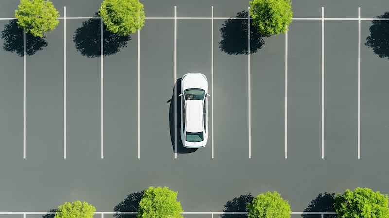 Overhead shot of a car in a parking lot, student driver performing a perfect parallel park, parking lines visible, sunny day