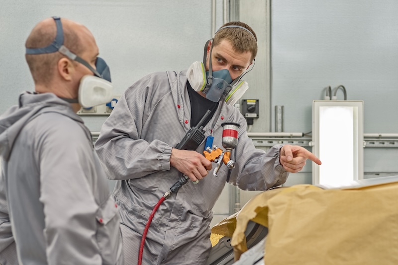 Employee of the paint shop of automobile factory carries out training in the painting of body parts with gun